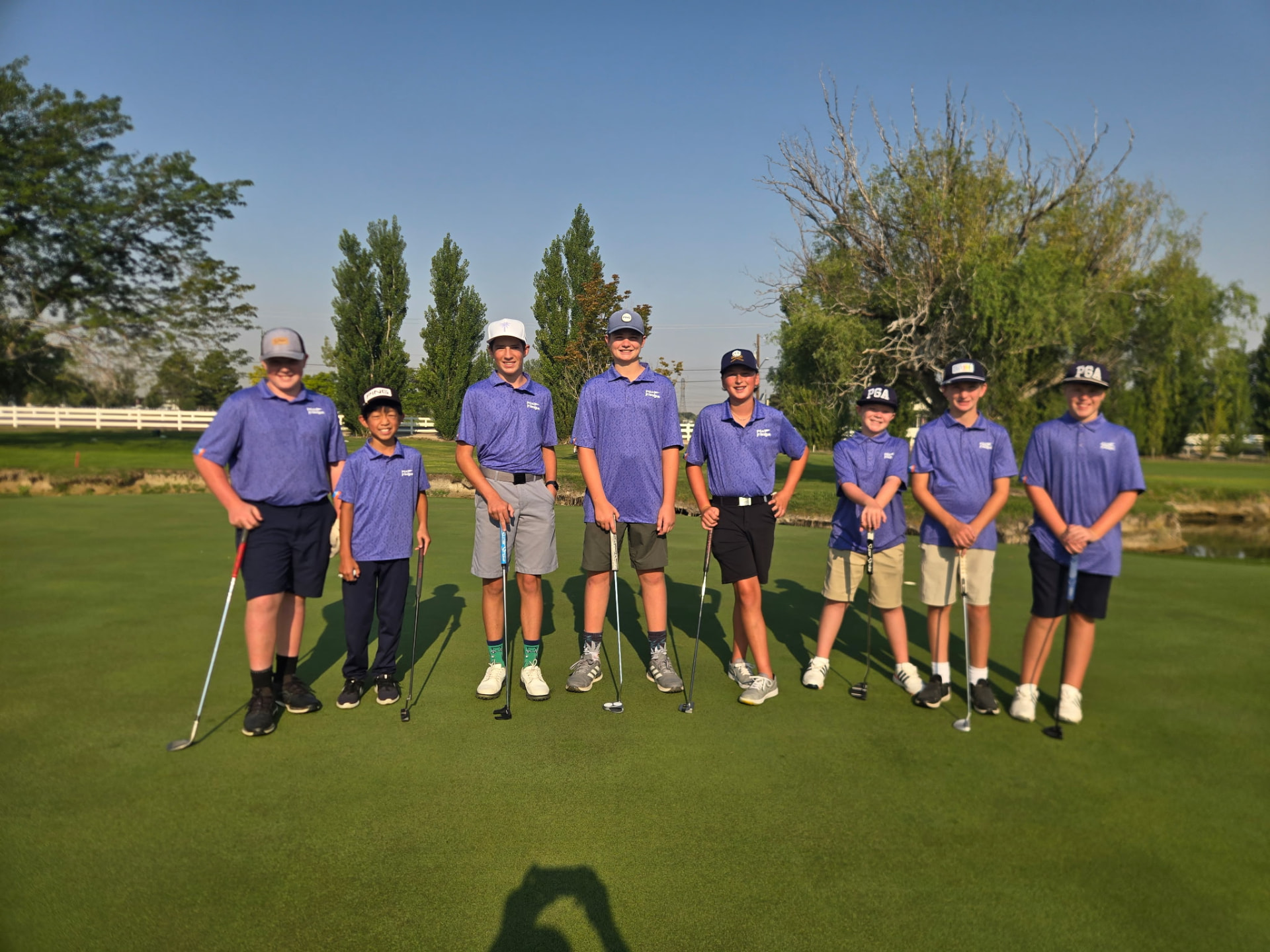 Junior golf team in matching purple polos standing on the putting green with their clubs
