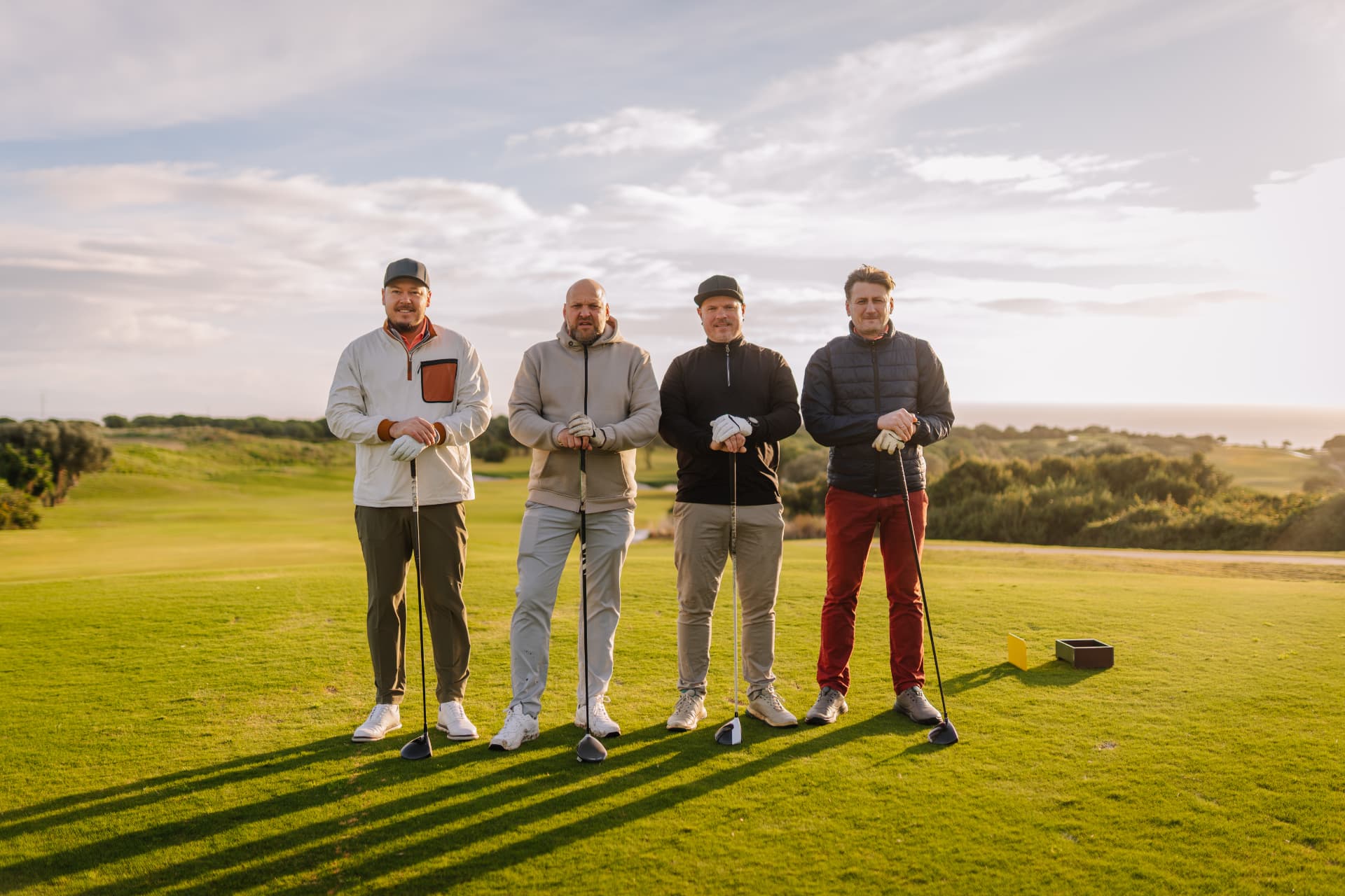 Four adult golfers standing with drivers on the tee box at sunset